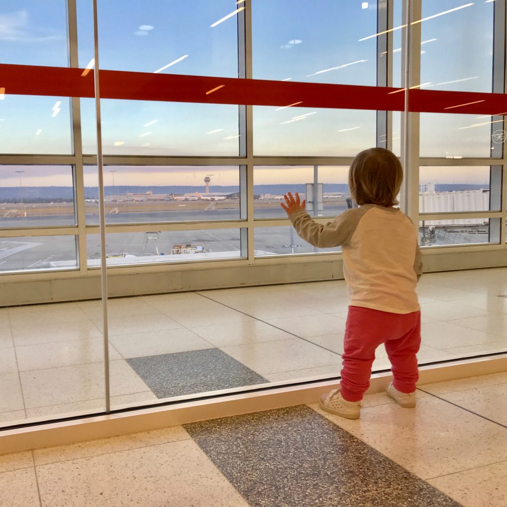 Baby standing by window in airport terminal watching the planes