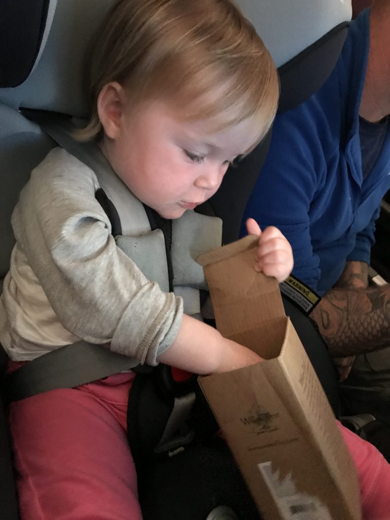 baby seated in car seat playing with simple cardboard box