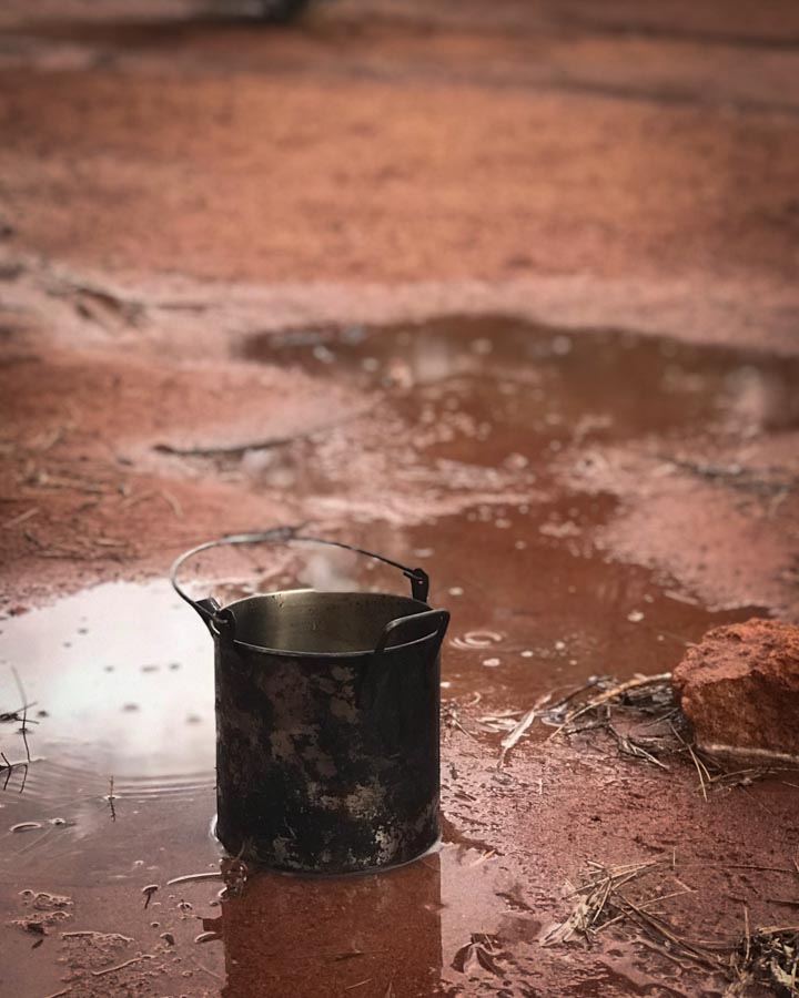 a metal kettle called a billy sitting in a puddle in the red dirt